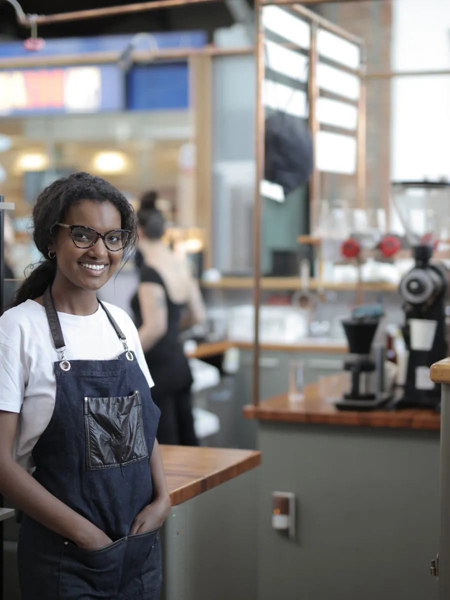 Smiling café owner in an apron standing behind her counter